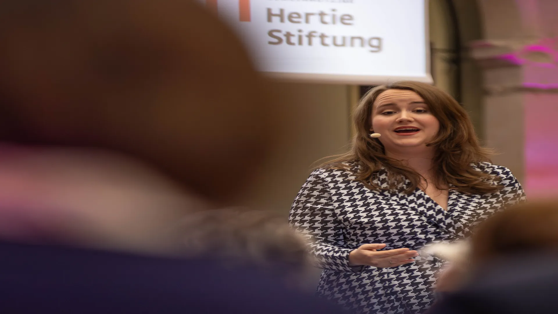 Politikerin Ricarda Lang spricht auf einer Bühne, im Vordergrund Publikum, im Hintergrund das Logo der Hertie-Stiftung 