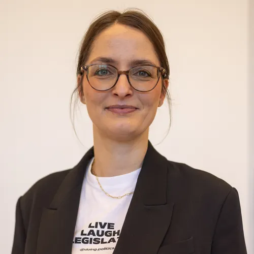 Portrait von Hanna Klein vor hellem Hintergrund, sie trägt ein Jackett und lächelt in die Kamera 