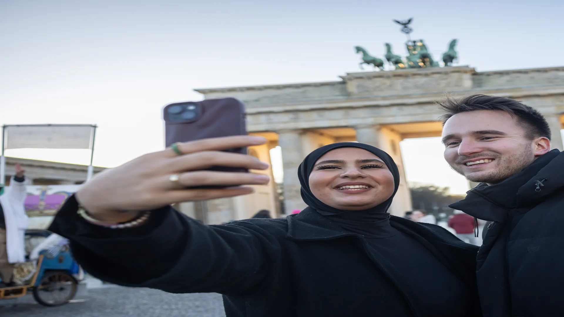 Eine junge Frau und ein junger Mann machen ein Selfie vor dem Brandenburger Tor in Berlin